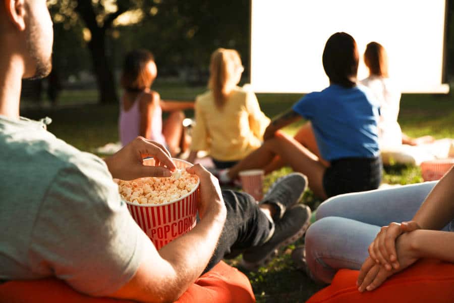 People holding popcorn and watching a movie outdoors at night