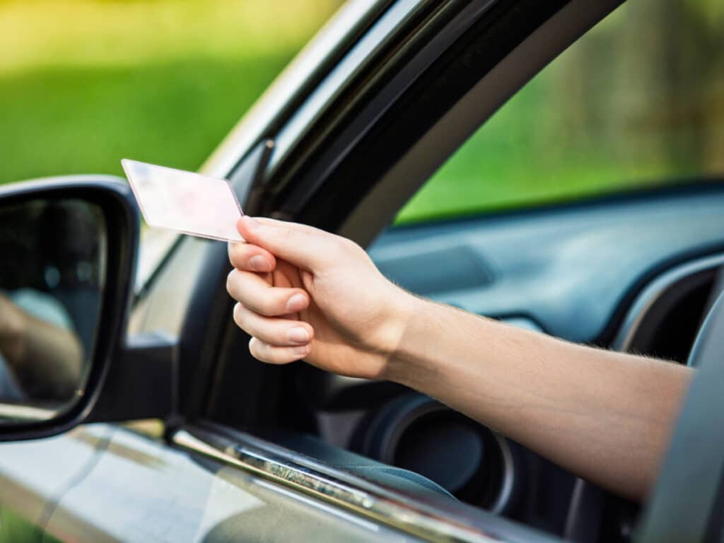 A hand handing out and ID card from the car