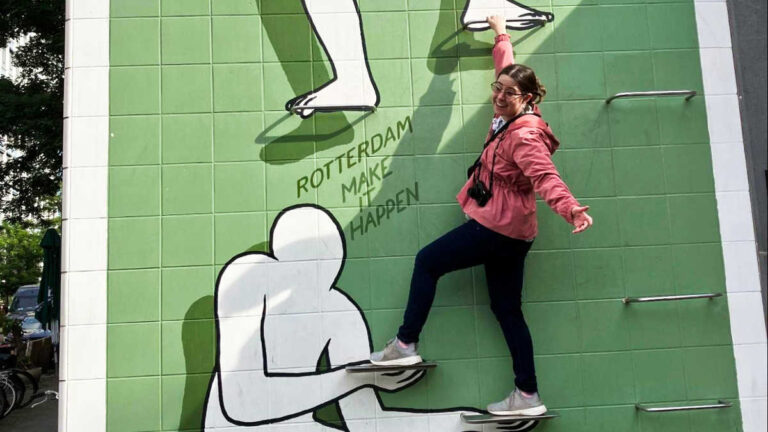 The author Meg O’Connor smiling for a photo while climbing on a street art in Rotterdam, Netherlands