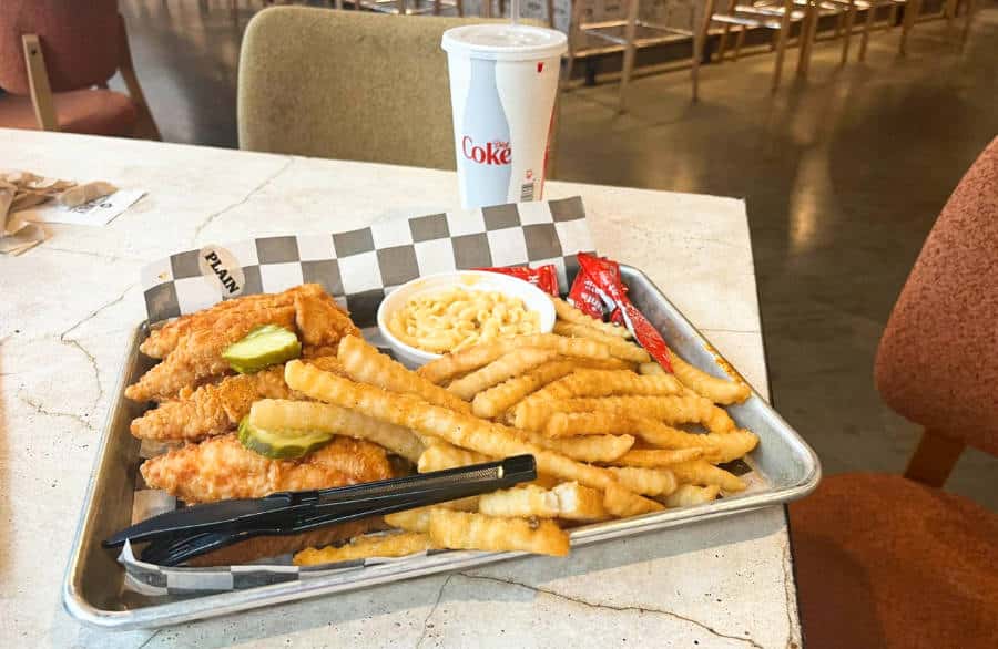 A tray full of fried chicken, fries, and different sauces with a cup of cola in Prince’s Hot Chicken
