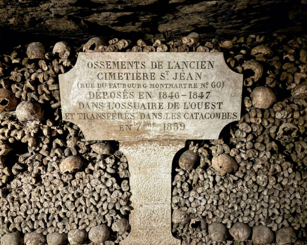 A stone plaque in the Paris Catacombs surrounded by stacked human skulls and bones