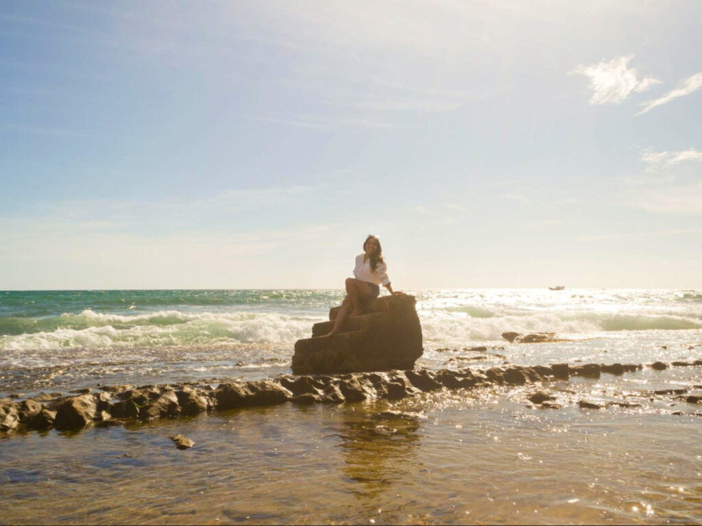 Author Vanessa Ramos sitting on a rock in the ocean at Playa Escalera