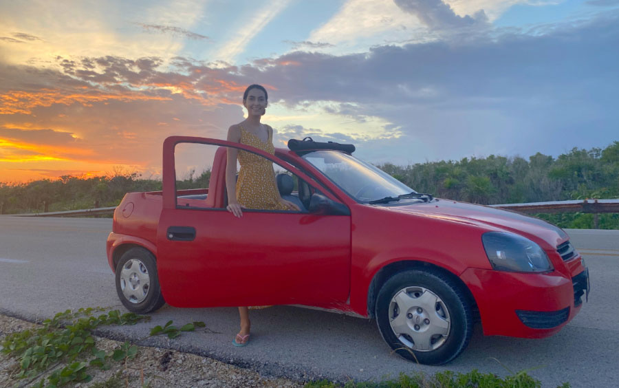 View of Clara in a convertible and the colorful sky with the sunset