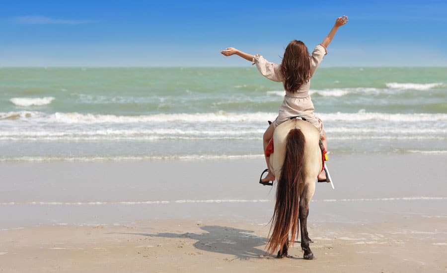 View of a woman riding a horse near the beach