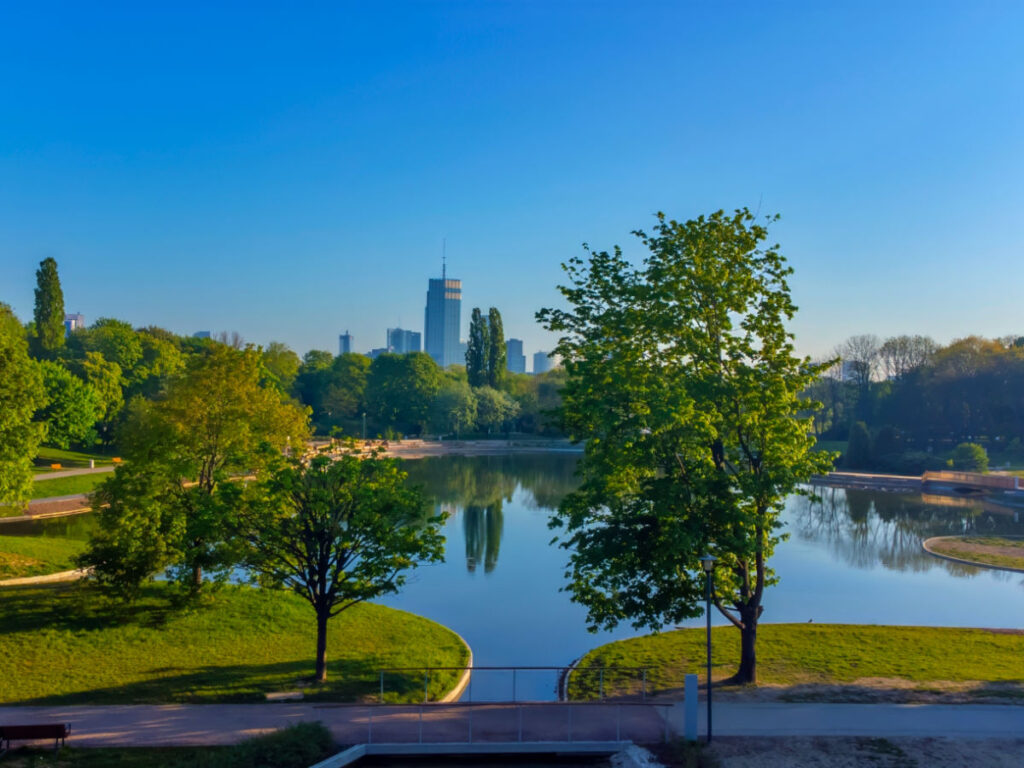 View of Pola Mokotowskie park, showcasing trees, a lake, and a city skyline in the distance