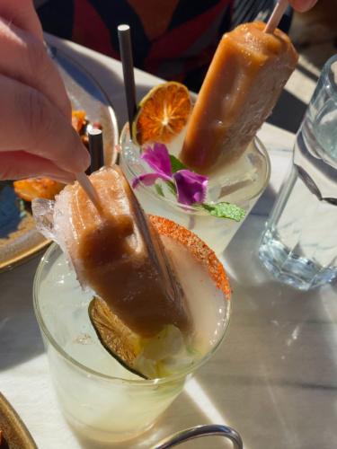 A person holding a Popsicle cocktail, a stick of ice cream dipping it in a cocktail