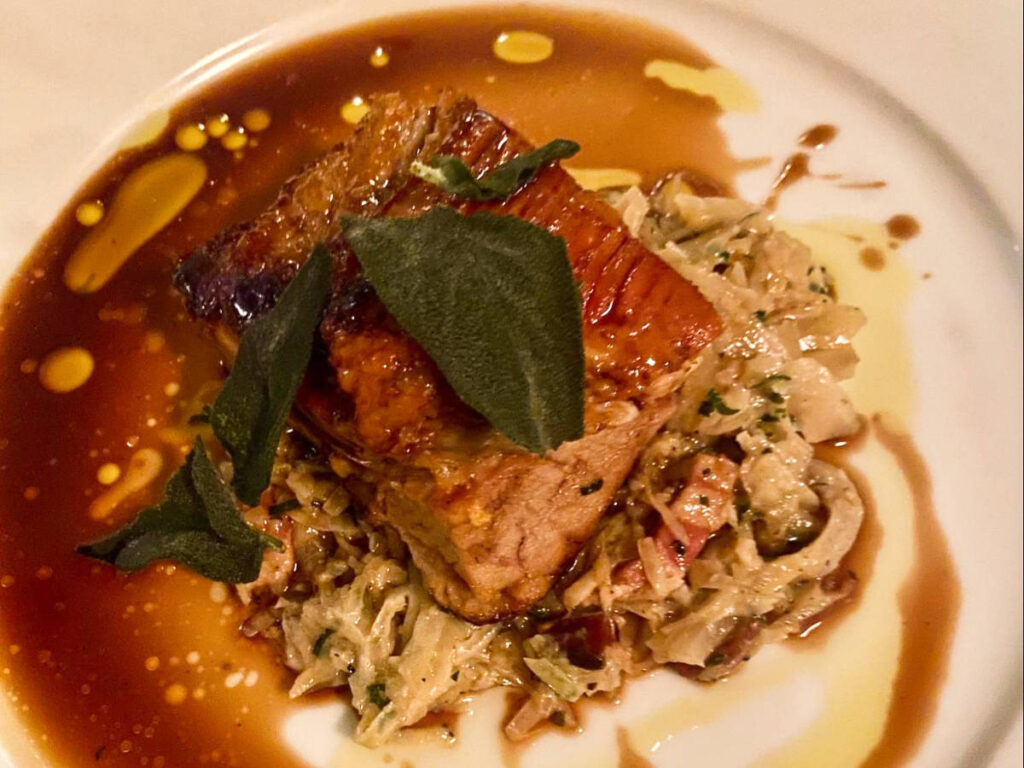 A plate of pork belly with crispy sage on a bed of vegetables and pancetta