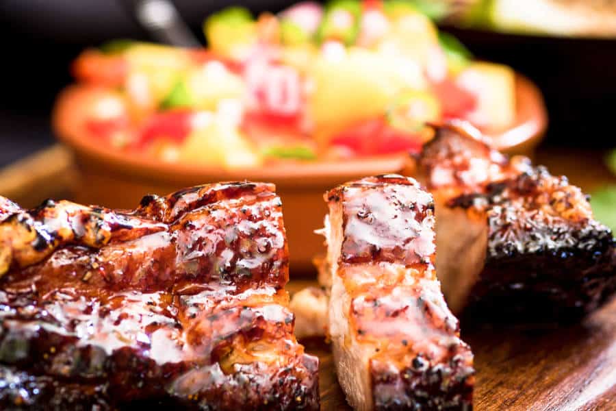 Closeup view of the grilled pork belly with mango salsa in the background
