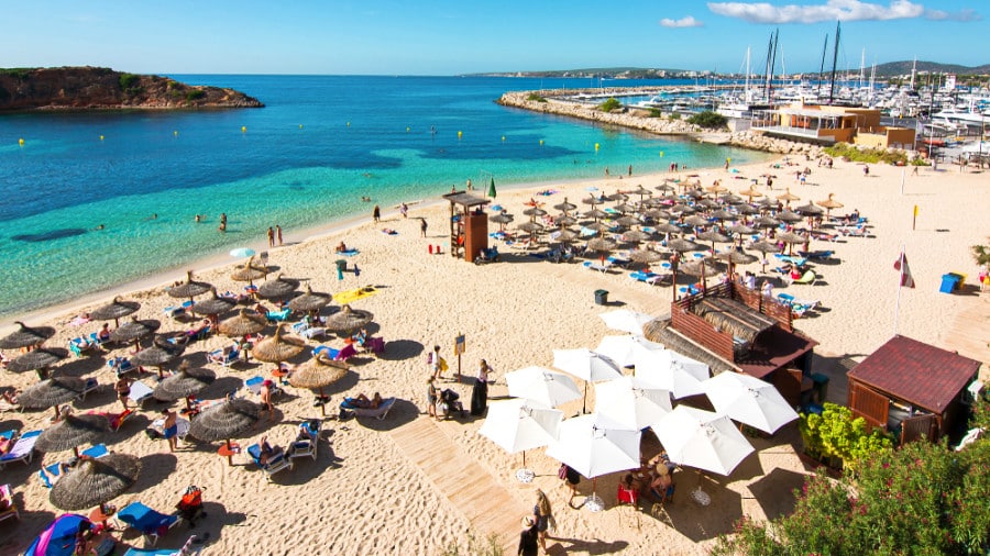 People enjoying under the umbrellas near the turquoise blue water of Portals Nous beach