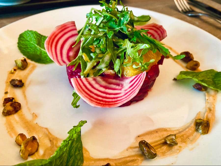 A plate of beef tartare topped with orange carpels and herbs and surronded with sauce, nuts and mint leaves