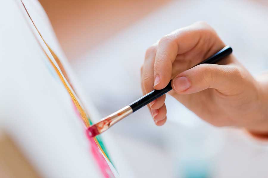 A hand holding a paint brush while painting an art on a canvas
