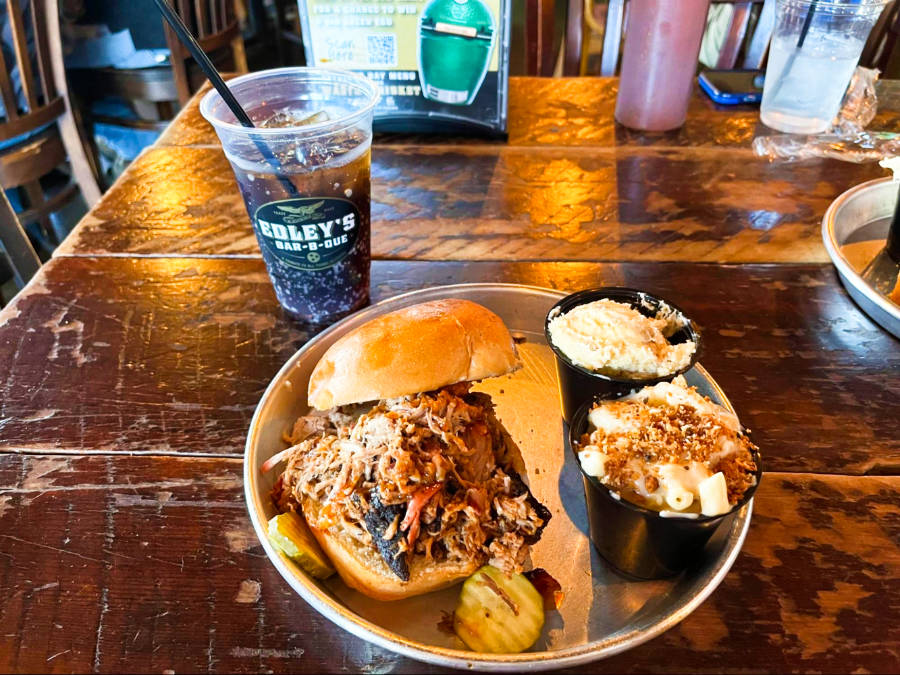 A plate of huge pulled pork sandwich and other dishes on the side with a cup of drink at Edley’s