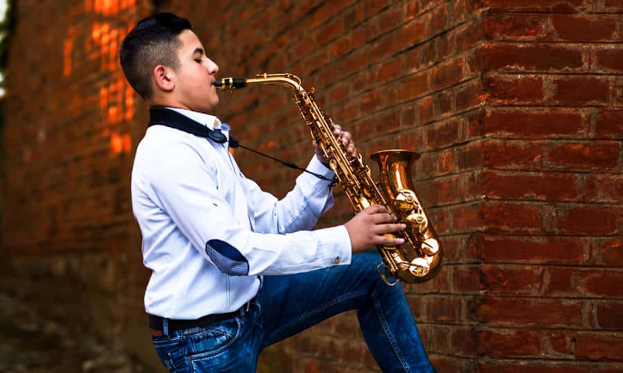 A man playing saxophone against a red brick wall.