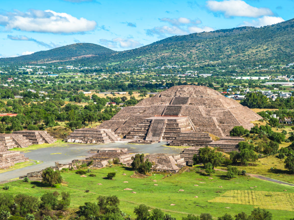 Aerial view of the Pyramid of the moon surrounded by greenery and mountain views in Teotihuacán
