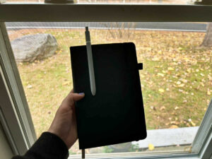 A hand holding the RETTACY journaling notebook with pen near the window