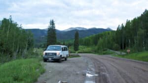 View of an RV along a dirt road with trees and mountains