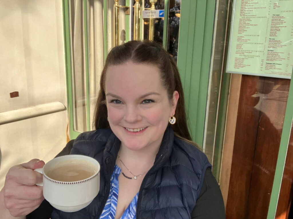The author Rachel Kapelke-Dale smiling for a photo while holding a cup of coffee