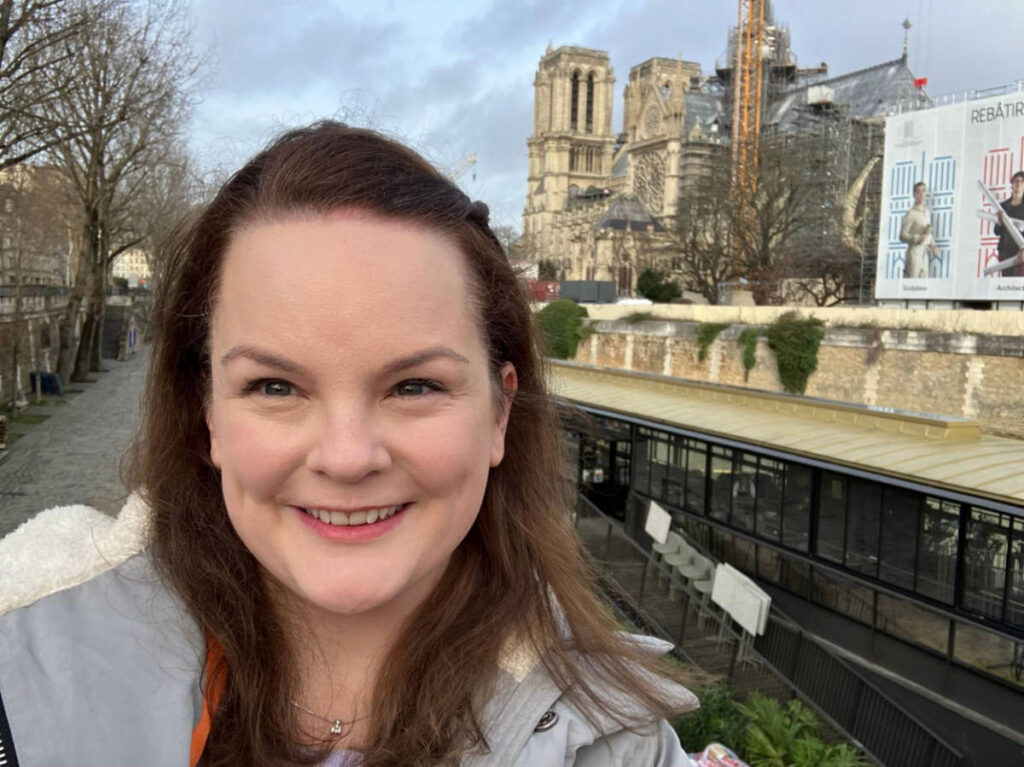 The author Rachel Kapelke-Dale smiling for a photo while walking to Notre Dame