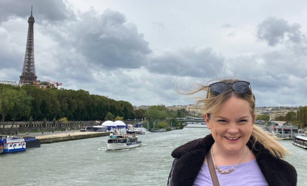 The author Rachel Kapelke-Dale smiling for a photo with the Eiffel Tower on her background
