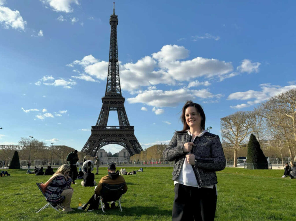 The author Rachel Kapelke-Dale posing for a photo at The Champ de Mars Park with the Eiffel Tower in the background