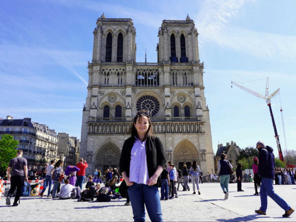 The author Rachel Kapelke-Dale posing for a photo in front of the Notre Dame de Paris Cathedral