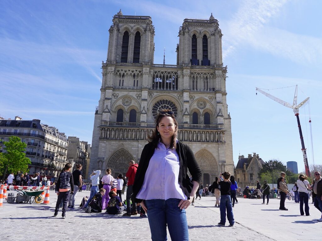 The author Rachel Kapelke-Dale posing for a photo in front of the Notre Dame de Paris Cathedral