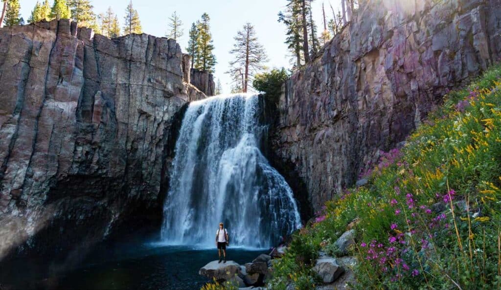 A man standing for a photo with the Rainbow Falls on his background