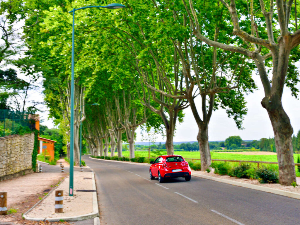 A red car driving along the the road in French countryside
