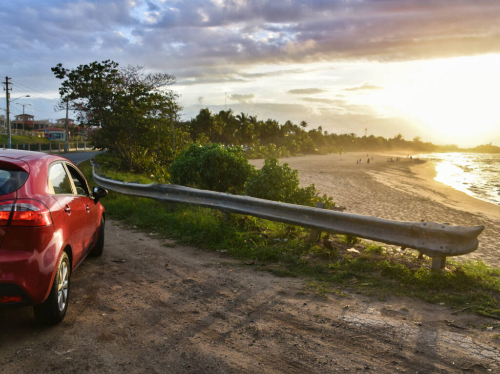 A red car parked at the beachfront at sunset