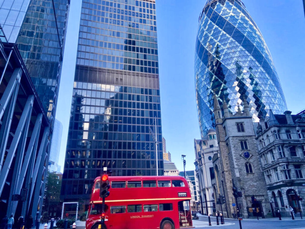 A red double-decker bus driving along the road with tall buildings around London