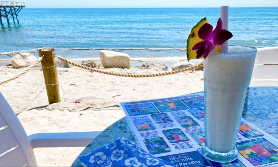 A smoothie topped with sliced pineapple and flower served on a table near the beach
