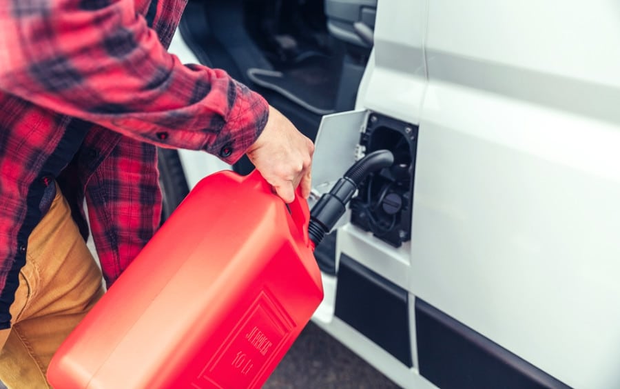 An arm of a man refueling a camper van with a red jerrycan