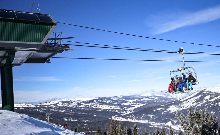 Skiers on a chairlift with a scenic view of the snowcapped Colorado Rocky Mountains in winter