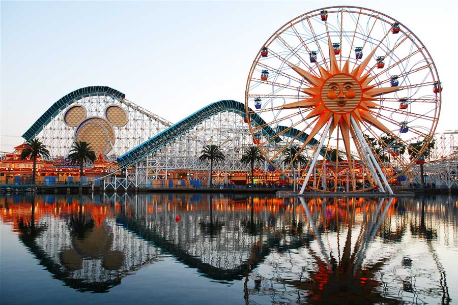Roller coaster and ferries wheel with a sun on it and the rides reflection on the lake