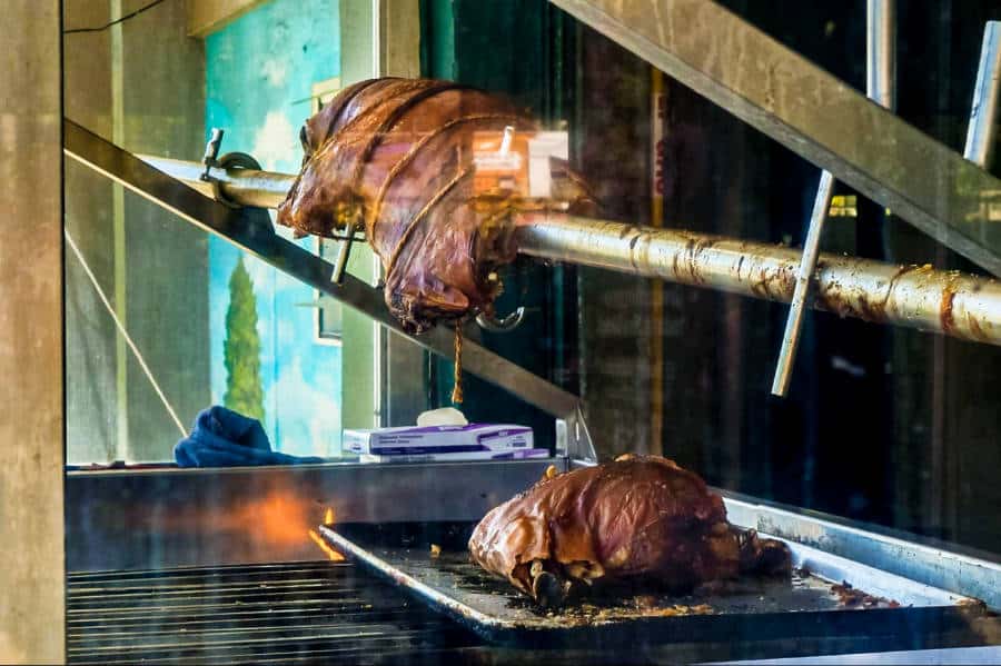 Two roasted pigs in a lechonera seen from the glass wall