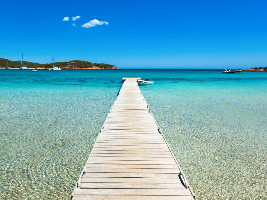 A long white pontoon over the turquoise blue water of Rondinara Beach with a clear blue sky in the background
