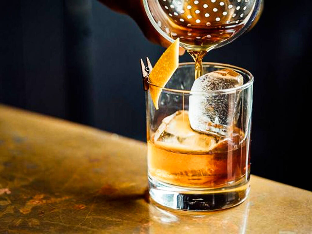 A hand pouring rum on a glass with ice cubes