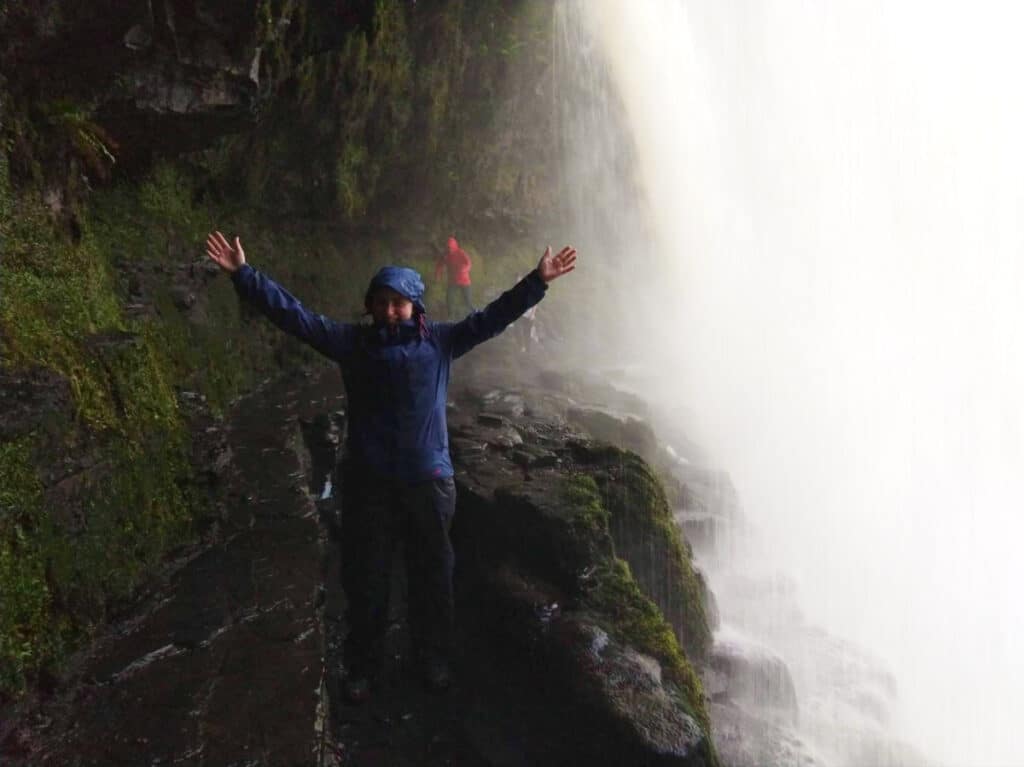 The author Ruth Elizabeth Walters, posing at the rocky path behind the Sgwd-yr-Eira waterfall