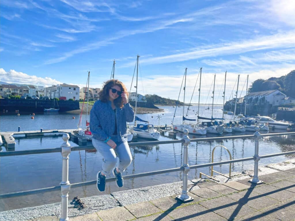 The author Ruthie Walters, posing for a photo while sitting on the railing at Porthmadog Harbour