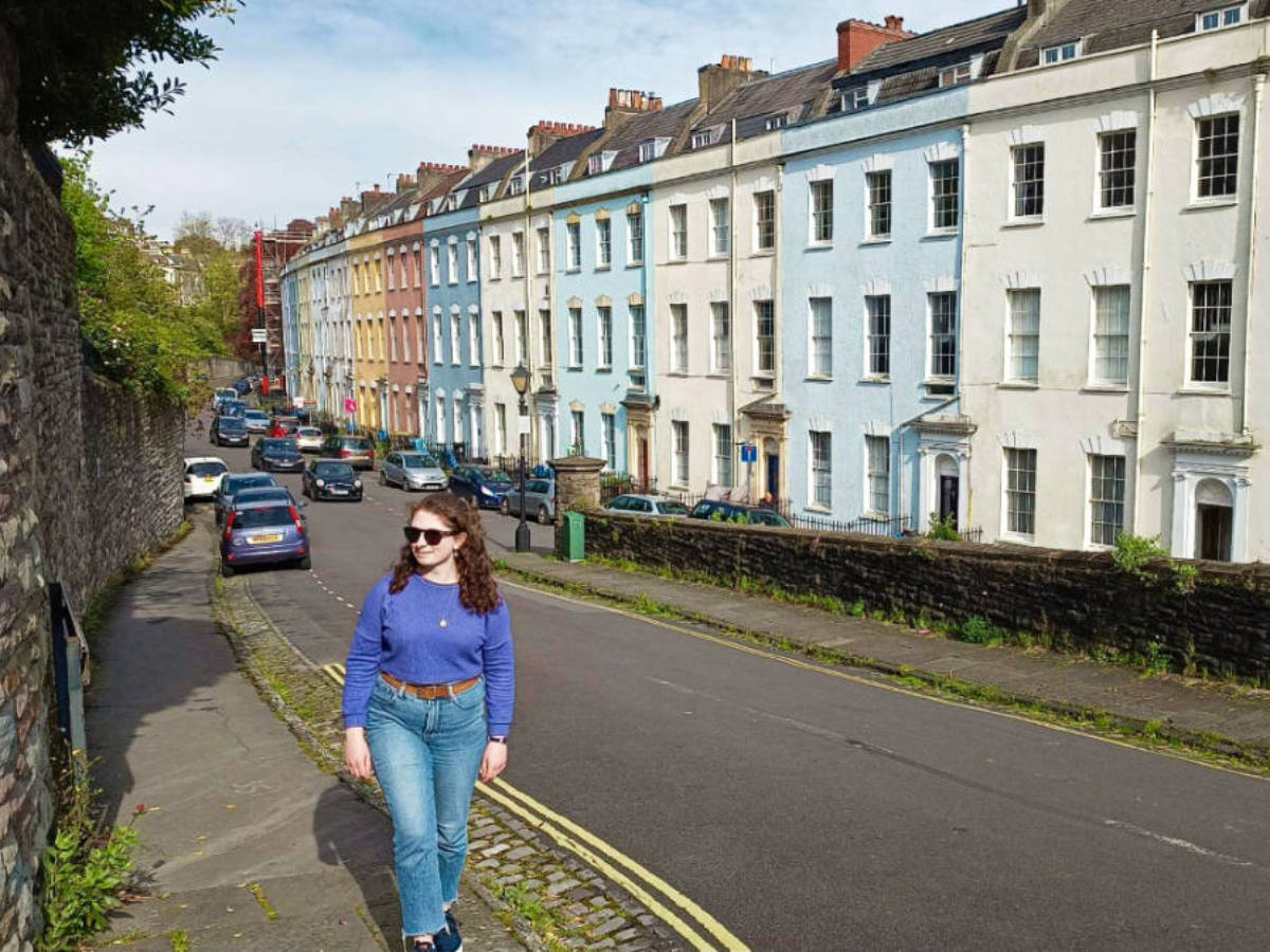 Travel Lemming writer Ruthie Walters walking across the street with the colorful buildings in the background in Clifton
