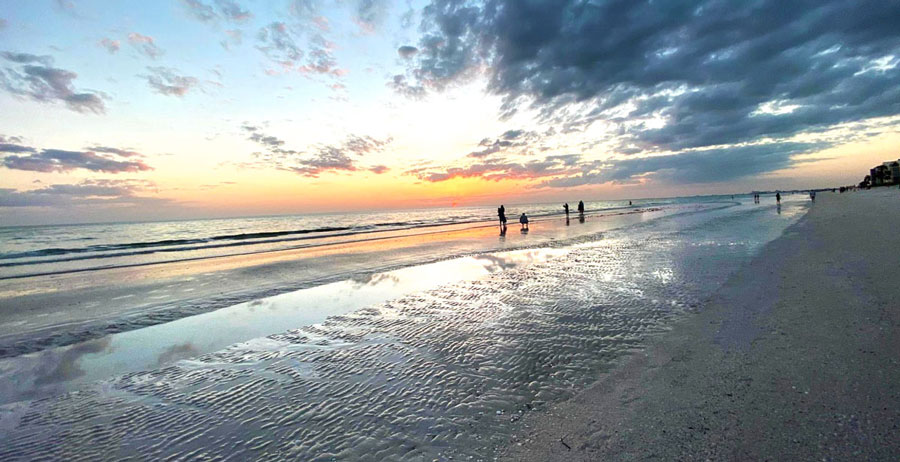 View of people by the beach and the colorful sky at sunset