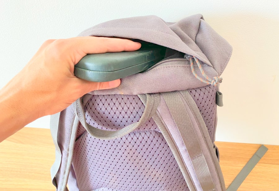 View of a hand inserting a glasses case into the top pocket of the Salkan daypack