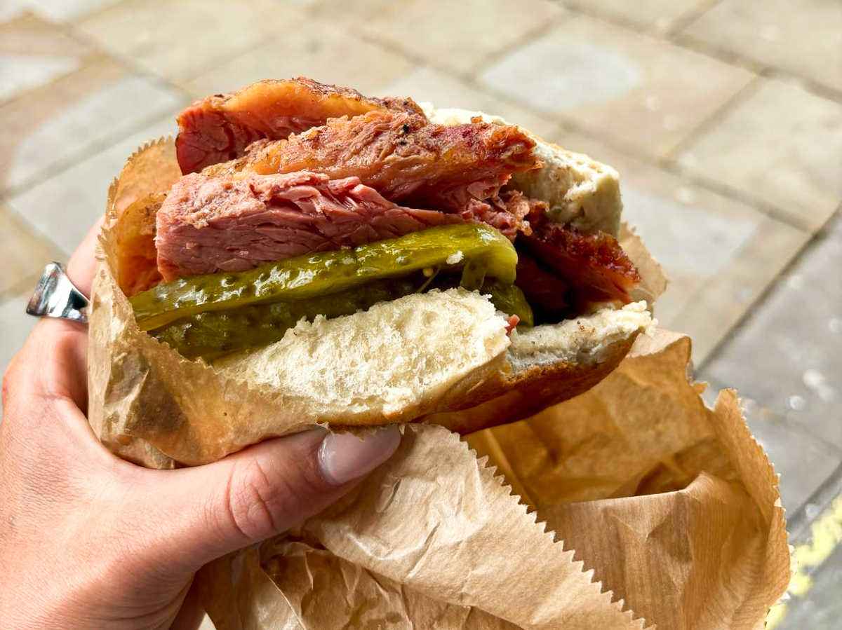 A hand holding a salt beef bagel sandwich