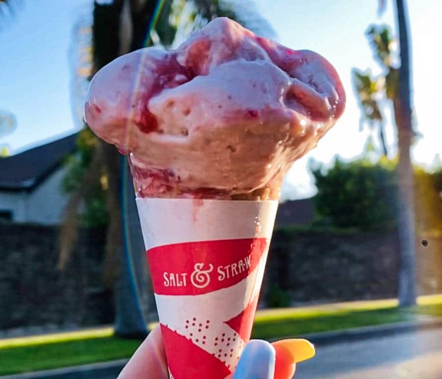 A semi-melted strawberry honey balsamic w/ black pepper ice cream in a cone