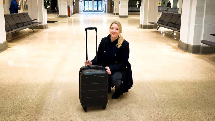 The author Taylor Herperger holding the Samsonite Omni PC Spinner Carry-On while squatting in the middle of the pathway