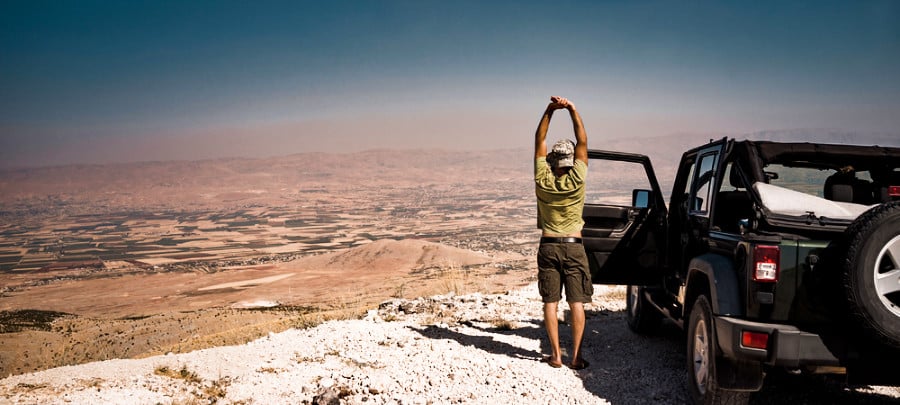A man stretching outside the car while enjoying the view below.