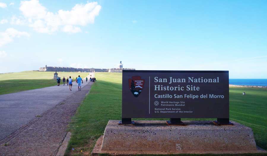 View of the sign for San Juan National Historic Site and tourists visiting it