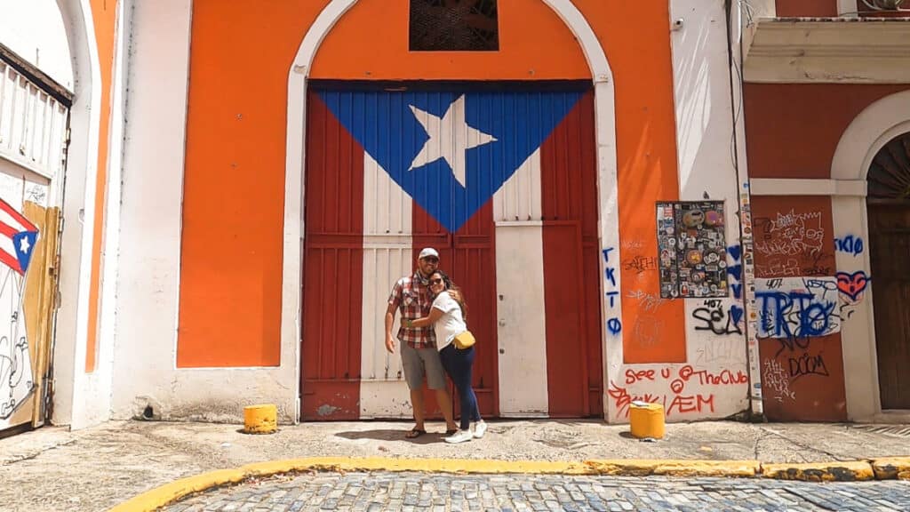 A couple posing on the vibrant colored wall with a huge Puerto Rican flag