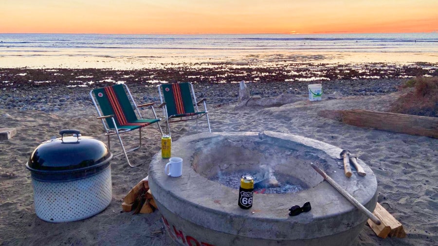 A bonfire pit, beer cans, and camping chairs at the shore of San Onofre Surf Beach during sunset