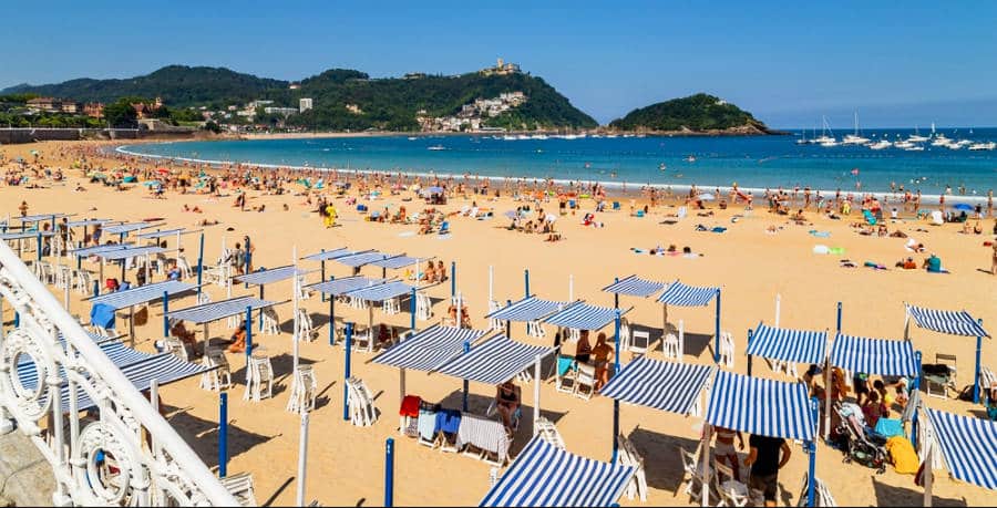 Landscape view of the crowded shoreline with umbrellas and chairs on San Sebastian's beach. 